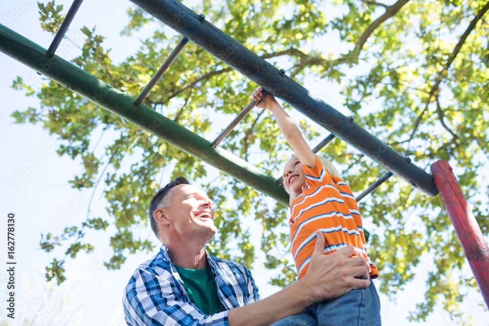 Fototapeta premium Father holding son playing on jungle gym at playground