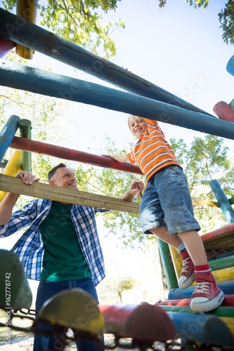 Happy father looking at son walking on jungle gym at playground photo