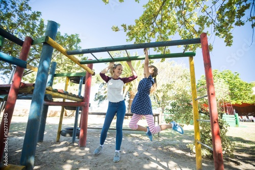 Happy mother talking to daughter hanging on jungle gym photo