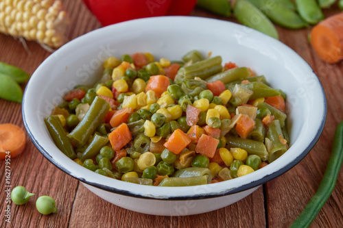 Mexican food stewed vegetables: carrots, green peas, asparagus, sweet peppers, corn. Organic vegetables on a wooden background.