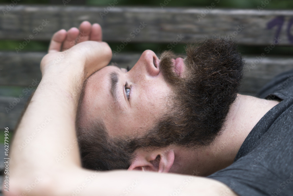 Obraz premium Handsome bearded guy resting laying on a bench in park