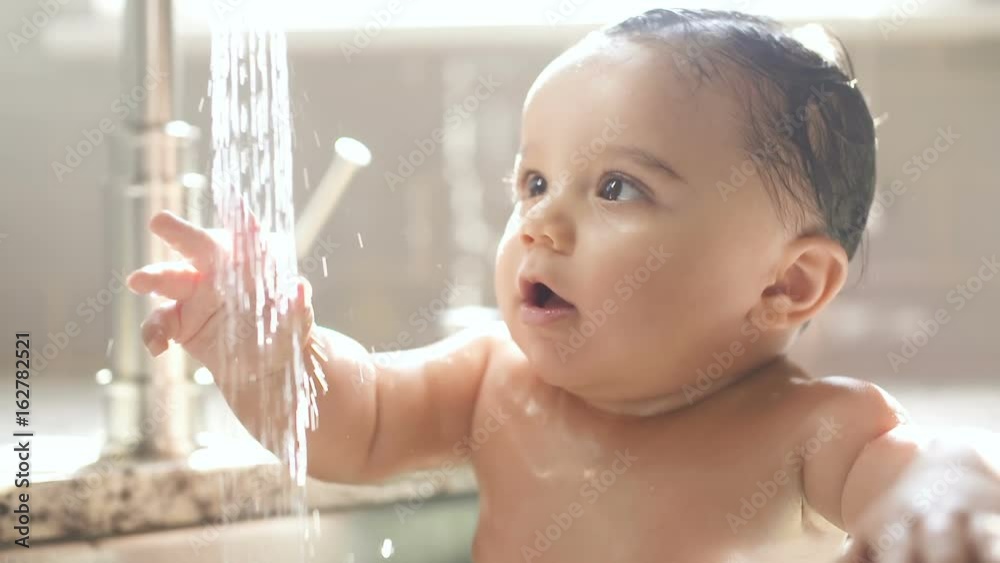 Baby in Awe of Water Stream from Sink Faucet. a stream of water pouring out of the faucet and baby looks at the water in amazement slow motion
