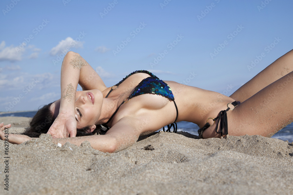 Beautiful sexy brunette in swimsuit with sequins lying on beach