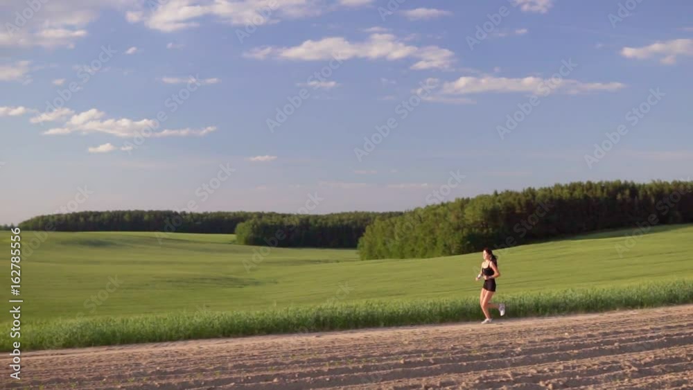 Young woman runner is runing across the field along the forest in a sporty uniform. Slow motion Young woman runner is runing across the field along the forest in a sporty uniform. Slow motion
