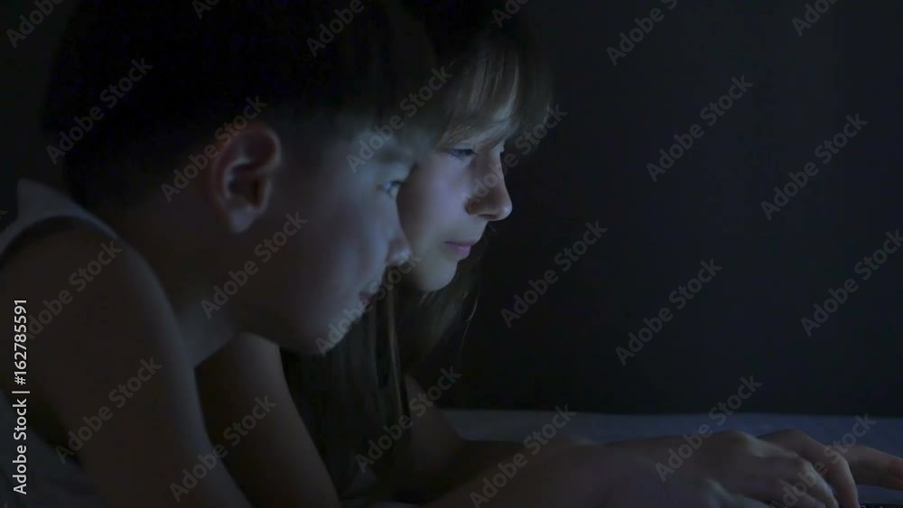 Children play on the computer in the bed under the blanket at night. Children play on the computer in the bed under the blanket at night.