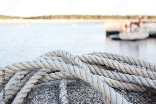 A close up of a dock rope, water surface and coast in the background.