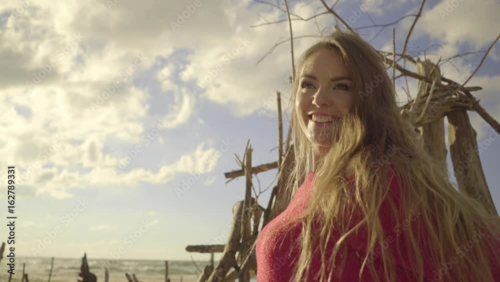 Summer girl outdoor on beach, cloudy sky background. Portrait of attractive happy woman tourist having fun with long hair blowing on wind. Carefree concept.