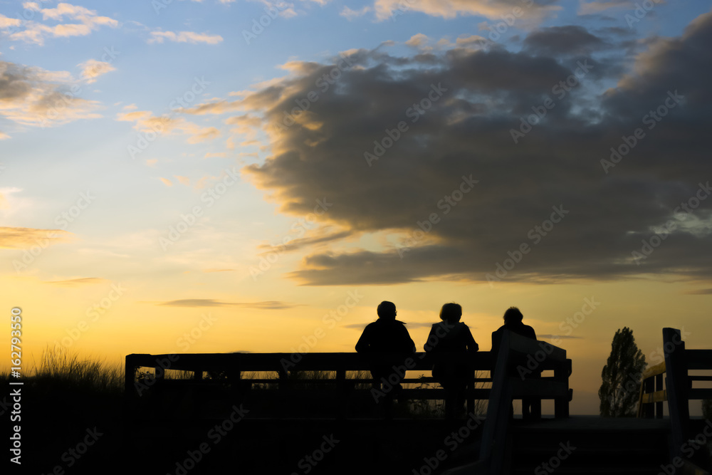 Three people sitting on bench and watching beautiful golden sunset