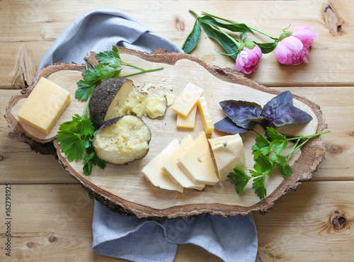 Assorted cheeses on wooden board with parsley, celery and little peony flowers, top view. Cheese heaven. 