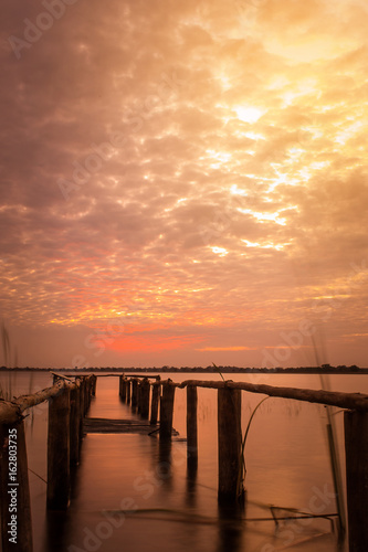 long exposure of wooden old bridge into the lake on the background of worm sky sunset.