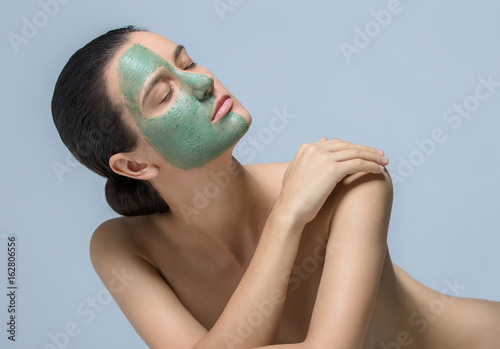 Young woman applaying green face mask - studio portrait photo