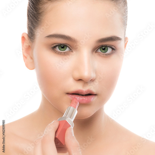 Portrait of beautiful young brunette woman with clean face. Beauty spa model girl with perfect fresh clean skin applying lipstick. Youth and skin care concept. Isolated on a white background.