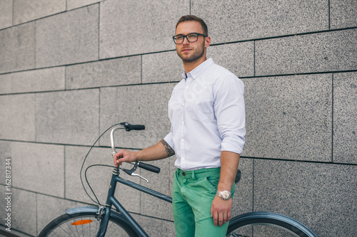 Confident business man with bike. Confident young handsome man in shirt and glasses holding bicycle while standing against white background