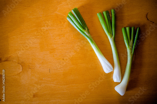 Three bunches of green onion on a brown wooden table
