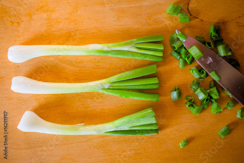 Three bunches, rings green onions and knife on table close-up