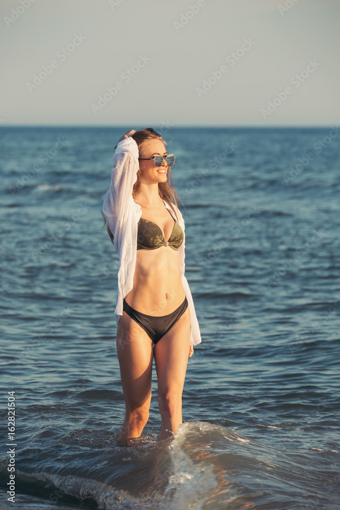 Attractive young woman walking along sea or ocean beach at sunset