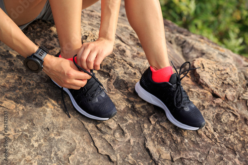 Young fitness woman trail runner tying shoelace at mountain top