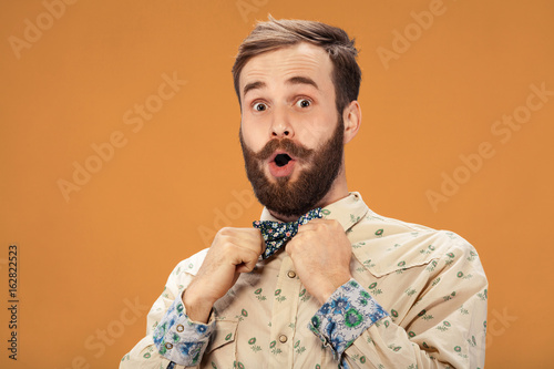Surprised happy man with beard and moustache looking sideways in excitement, isolated on orange background