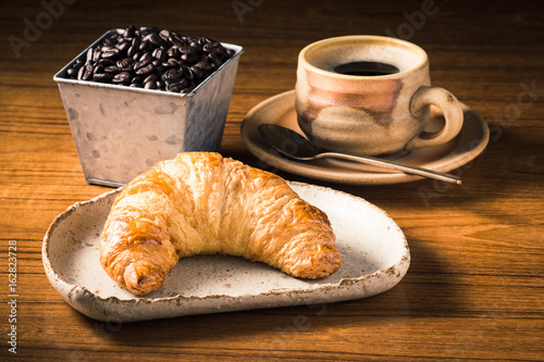 butter croissant in dish on wooden table with espresso cup and coffee bean bucket at back