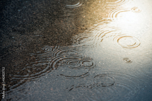 Fotografie, Obraz in drops rippling in a puddle with blue sky reflection.