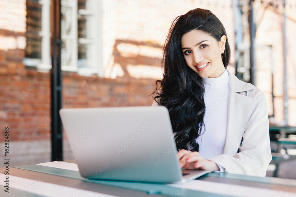 Attractive female blogger typing new challenging post using modern laptop computer while sitting at outdoor cafe. Pretty brunette businesswoman working with laptop doing her business project Attractive female blogger typing new challenging post using modern laptop computer while sitting at outdoor cafe. Pretty brunette businesswoman working with laptop doing her business project