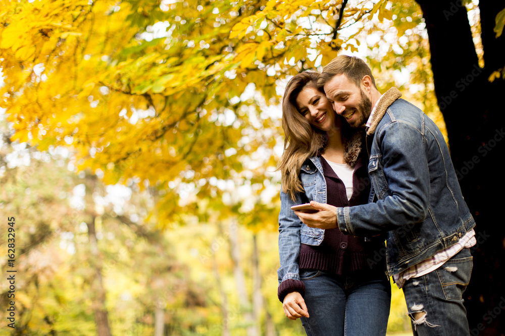 Happy couple watching a smart phone and standing in autumn park Happy couple watching a smart phone and standing in autumn park