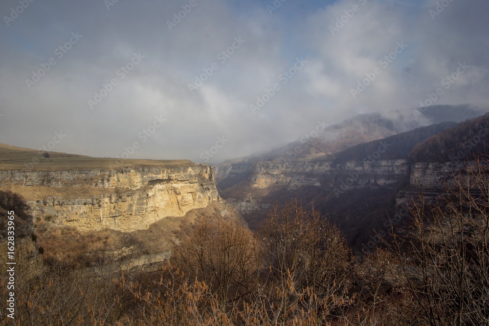 Горный пейзаж. Красивый вид на высокие скалы в живописном ущелье. Солнечная погода. высокие горы в облаках, природа и горы Северного Кавказа