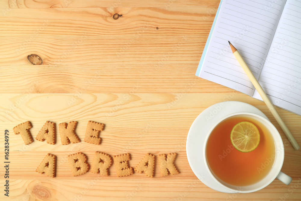 Hot Lemon Tea, Note Papers and Pencil beside with Word TAKE A BREAK Spelling with Cookies on Wooden Table Hot Lemon Tea, Note Papers and Pencil beside with Word TAKE A BREAK Spelling with Cookies on Wooden Table