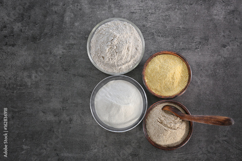 Bowls with different types of flour on gray background