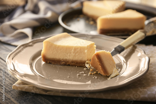 Plate with delicious cheese cake and spoon on kitchen table