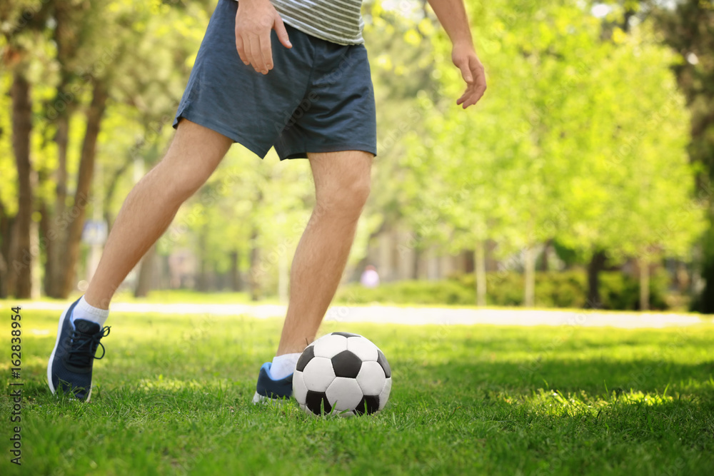 Young man playing football on green grass in park Young man playing football on green grass in park