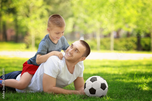 Father and son with soccer ball lying on green grass in park