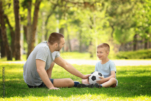 Father and son playing with soccer ball on green grass in park © Africa Studio