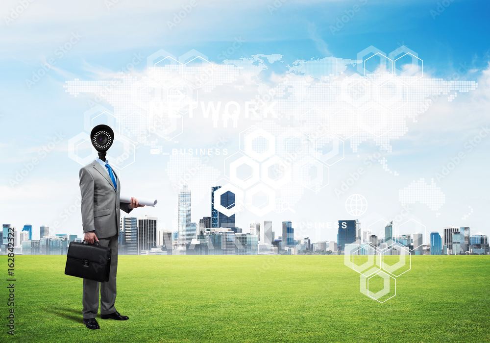 Camera headed man standing on green grass against modern cityscape