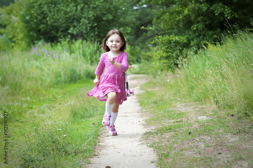 Adorable little girl in pink dress runs in the forest. Sunny day © Tanya