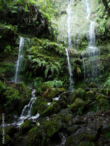 Narrow white stream of water flows as waterfall over a stone cliff until it splashes on the bedrock. The rock face is wetted by water running down the wall in several little trickles.