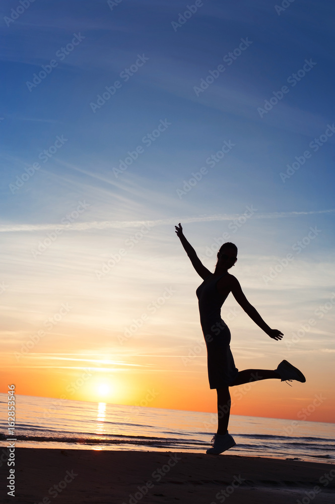 Enjoying the summer sunset. Cheerful woman silhouette dancing on beach.