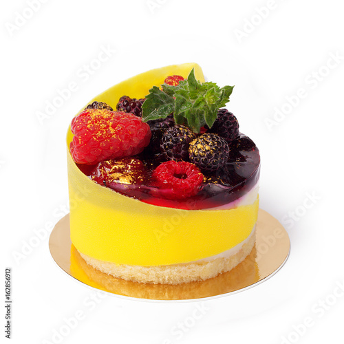 Modern french mousse cake with fresh blackberries, raspberries and branch of mint isolated on white. Biscuit and jelly dessert decorated of yellow edible wrapper and golden powder closeup.