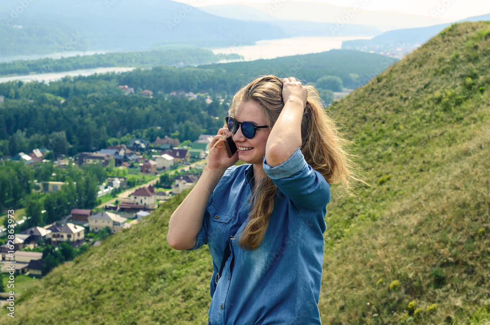Young girl in blue clothes talking on the phone in the background of a beautiful landscape