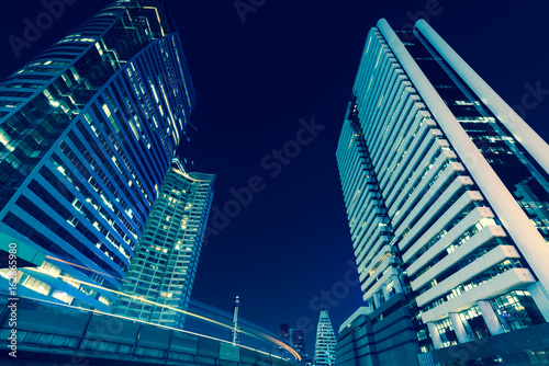 Photo of commercial office buildings exterior. Night view at bottom skyscrapers with light of traffic rush, long exposur in Bangkok