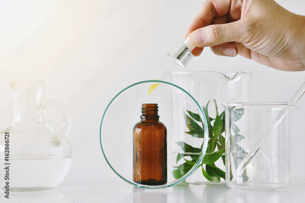 Cosmetic brown bottle containers and scientific glassware, Focus on oil dropping in blank label package for branding mock-up, Research and develop beauty skincare product concept.