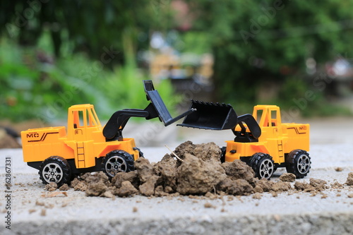 Truck toy car with sand and soil on the concrete floor with blur boken green environment construction equipment at work ,construction concept, selective focus.