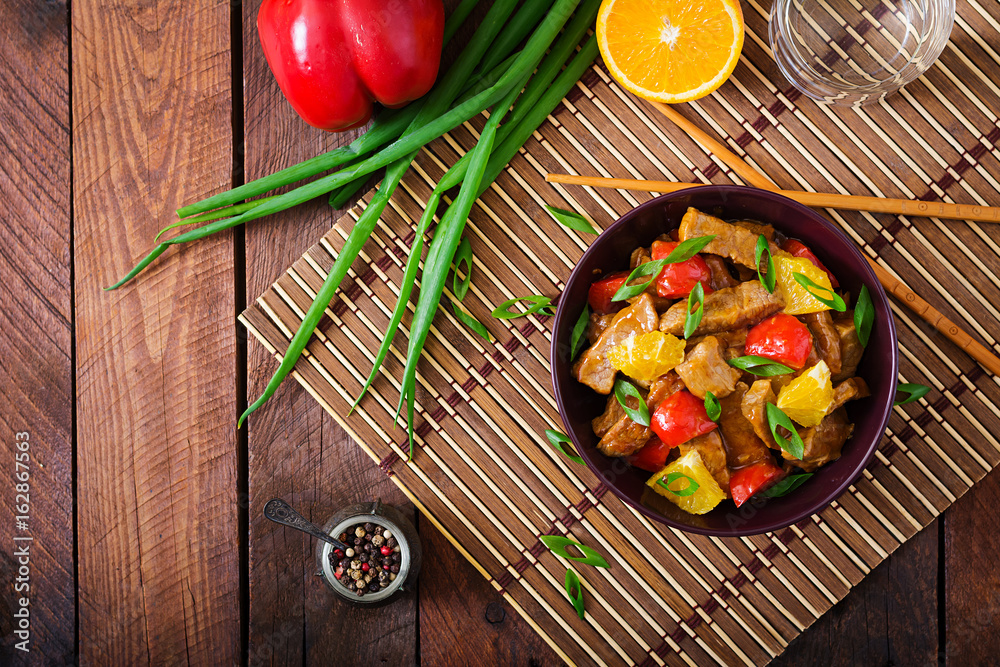 Veal fillet - stir fry with oranges and paprika in sweet and sour sauce on a wooden background. Flat lay. Top view Veal fillet - stir fry with oranges and paprika in sweet and sour sauce on a wooden background. Flat lay. Top view