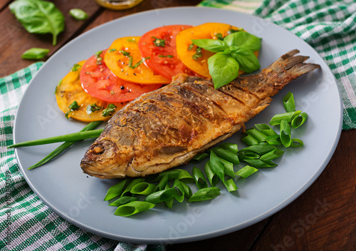 Fried fish carp and fresh vegetable salad on wooden background.