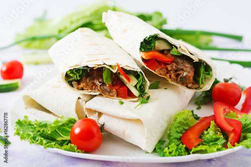 Burritos wraps with minced beef and vegetables on a light background. photo