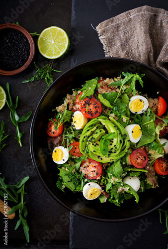 Diet menu. Healthy salad of fresh vegetables - tomatoes, avocado, arugula, egg, spinach and quinoa on a bowl. Flat lay. Top view.
