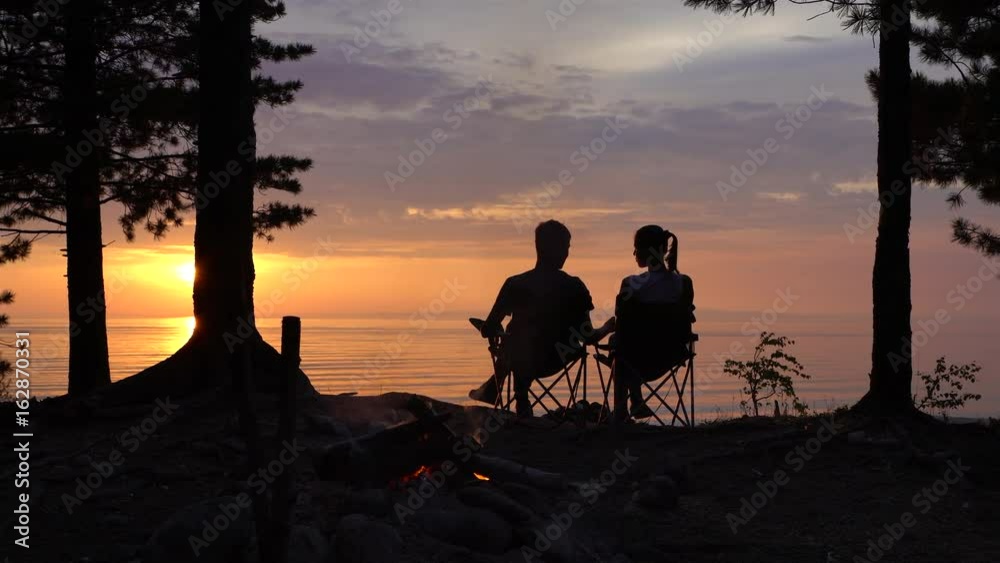 Couple is Sitting near Campfire at Night. Couple is Sitting near Campfire at Night.