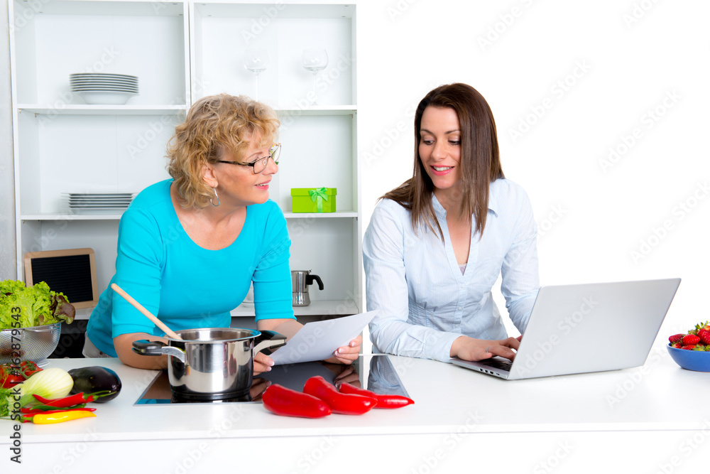 young woman and her mother together in the kitchen and using laptop young woman and her mother together in the kitchen and using laptop