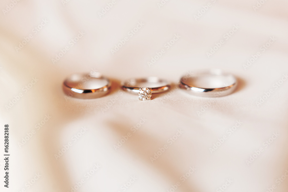 Set of three golden rings on silk textile - engagement ring with diamond and pair of wedding rings. Symbol of love and marriage. Set of three golden rings on silk textile - engagement ring with diamond and pair of wedding rings. Symbol of love and marriage.