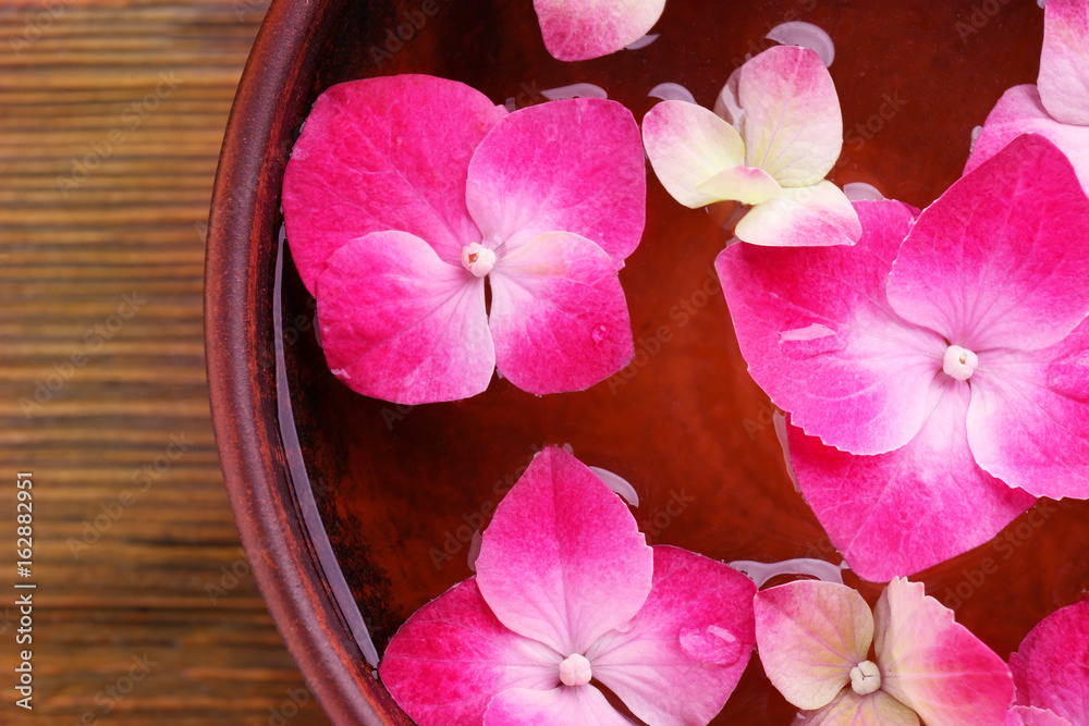 Bowl with water and hortensia flowers on wooden background, close up Bowl with water and hortensia flowers on wooden background, close up